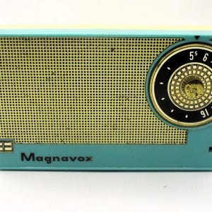 May include: A teal and yellow vintage Magnavox transistor radio with a black dial and gold numbers. The radio has a speaker grille on the front.