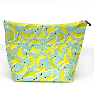 May include: A zippered cosmetic bag with a light blue background and a repeating pattern of yellow bananas and banana peels. The bag has a yellow zipper lining and a black zipper pull.