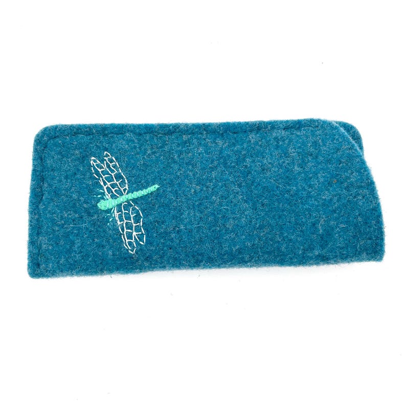 May include: A rectangular teal felt case featuring an embroidered dragonfly design. The dragonfly has a light green body and white stitched wings. The case is constructed from a textured, dense felt material with visible stitching along the edges.