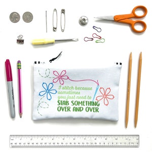 May include: A white zippered pouch with the text "I stitch because sometimes you just need to STAB SOMETHING OVER AND OVER" in colorful embroidery. The pouch is surrounded by various sewing supplies, including needles, pins, scissors, a ruler, and two wooden knitting needles.