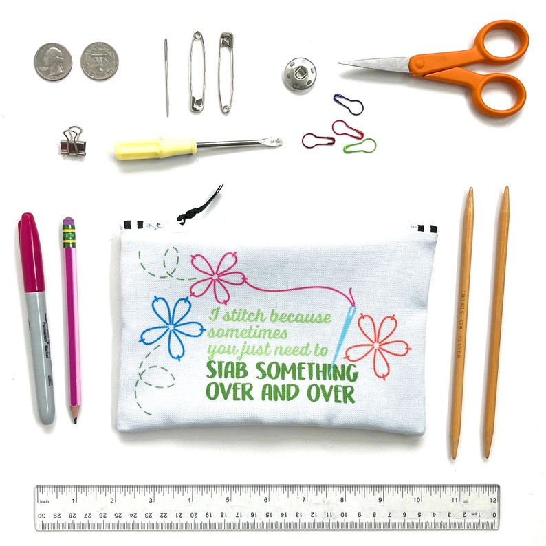 May include: A white zippered pouch with the text "I stitch because sometimes you just need to STAB SOMETHING OVER AND OVER" in colorful embroidery. The pouch is surrounded by various sewing supplies, including needles, pins, scissors, a ruler, and two wooden knitting needles.