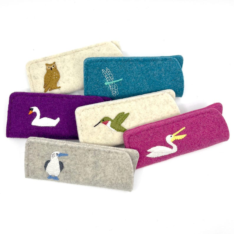 May include: A collection of six rectangular felt cases in various colors including cream, teal, purple, and gray. Each case features a small embroidered animal or insect design, specifically an owl, dragonfly, swan, hummingbird, pelican, and booby bird.
