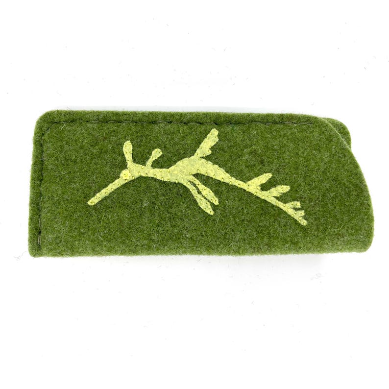 Op de afbeelding: Een rechthoekig etui van olijfgroen vilt met een geborduurde lichtgele zeedraak-silhouet op de voorzijde. Het etui heeft zichtbare donkergroene stiksels langs de bovenrand en een gevouwen constructie met een zachte, getextureerde afwerking.