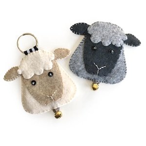 May include: Two felt sheep keyrings with black eyes and bells. One sheep is white and the other is grey.
