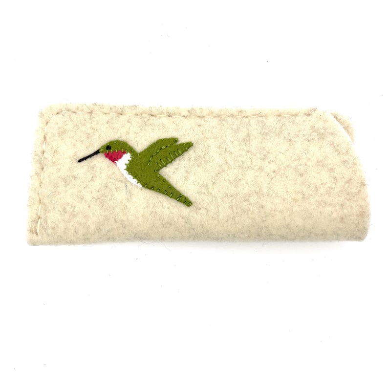 May include: A rectangular beige felt case featuring an embroidered hummingbird design. The bird is depicted in profile with green wings, a white chest, and a small red patch near the throat, finished with a thin black beak and visible stitching.
