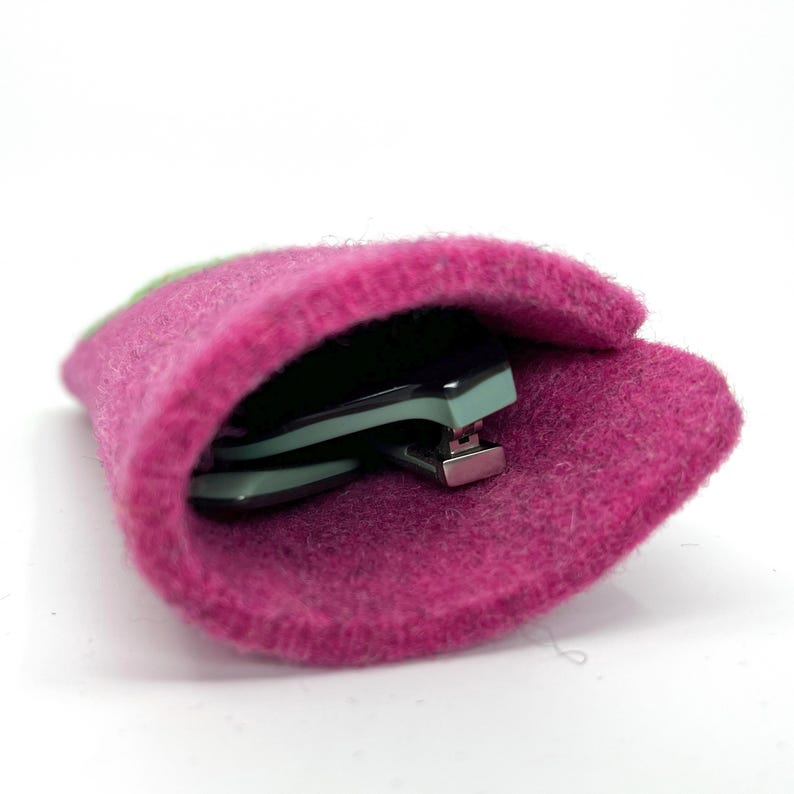 Op de afbeelding: Een fel magenta viltzakje met een zacht, getextureerd oppervlak. Binnenin de opening van het zakje is een opgevouwen bril met licht muntgroene monturen en zilverkleurige metalen scharnieren gedeeltelijk zichtbaar in de hoes geplaatst.