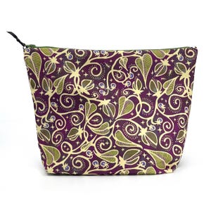 May include: A zippered pouch featuring a deep purple background with a repeating pattern of light green and cream-colored stylized carnivorous plants, vines, small berries, and tiny ants, finished with a green zipper and a black pull tab.