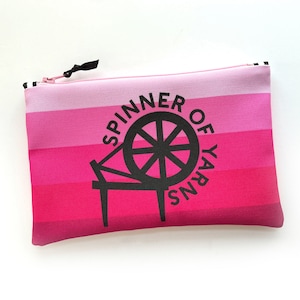 May include: Pink and white striped zippered pouch with a black spinning wheel graphic and the text "Spinner of Yarns".