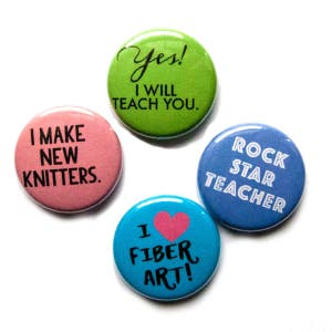 May include: Four 1-inch button pins with different designs. The first pin is pink and says "I make new knitters." The second pin is green and says "Yes! I will teach you." The third pin is blue and says "Rock star teacher." The fourth pin is blue and says "I fiber art!" with a pink heart.