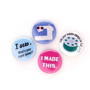May include: Four colorful button pins with sewing-themed designs. One pin features a sewing machine with sunglasses, another has a spool of thread, one says "I sew. What's your super power?" and the last one says "I MADE THIS."