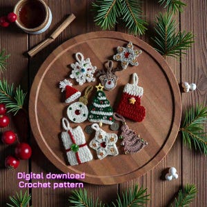 Op de afbeelding: Een verzameling handgemaakte gehaakte kerstversieringen in verschillende vormen, waaronder een boom, een sneeuwvlok en een kous, gerangschikt op een houten dienblad. De ornamenten zijn wit, rood en groen, met decoratieve kralen. De tekst "Digital download Crochet pattern" is zichtbaar.