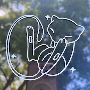 May include: White outline of a cartoon cat-like creature in a curled pose, with three small star shapes around it. The design is on a dark surface, possibly a window or sticker.