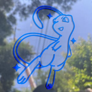 May include: A blue and white decal of the Pok&eacute;mon Mew, with a stylized design. The decal features a smiling Mew with a long tail and three star accents. The image is set against a blurred background of a window and trees.