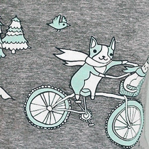 May include: A gray t-shirt with a graphic of a dog riding a bicycle through a forest. The dog is wearing a scarf and there are two trees and a bird in the background. The text "boygirlparty&reg;" is printed on the shirt.