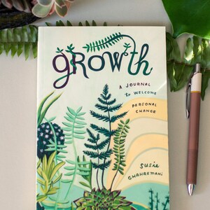 May include: A green, yellow, and white journal with the word "growth" in a stylized font. The journal is decorated with illustrations of plants and ferns. The text "A journal to welcome personal change" is printed on the cover. The author's name, "Susie Ghahremani", is printed at the bottom of the cover.