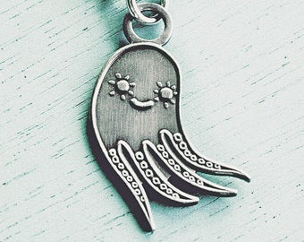 Op de afbeelding: Zilverkleurige ketting met een hanger in de vorm van een lachende octopus. De octopus heeft gestileerde ogen en tentakels met kleine cirkelvormige details. De ketting hangt aan een kogelketting, tegen een lichtblauwe achtergrond.