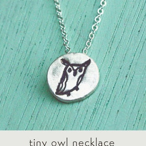 May include: A silver necklace with a small, round pendant featuring a black owl illustration. The necklace is displayed on a turquoise surface. The text "tiny owl necklace" and the copyright symbol are also visible.