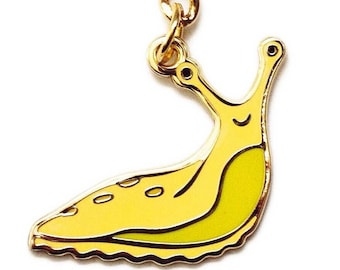 May include: A gold-colored keychain featuring a yellow banana slug with a smiling face. The keychain has a gold-colored ring and chain.