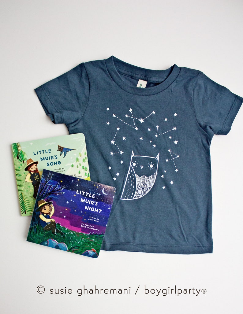 May include: Two children's books titled "Little Muir's Song" and "Little Muir's Night" with illustrations of children in nature. A blue t-shirt with a white owl and stars printed on it.