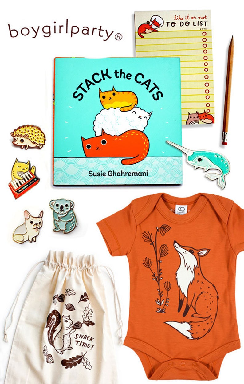 May include: A set of baby items including a book titled "Stack the Cats" by Susie Ghahremani, a light orange bodysuit with a fox graphic, a white drawstring bag with a squirrel graphic and the text "Snack Time!" and a variety of enamel pins.