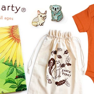 Op de afbeelding: Een set babycadeaus, waaronder een boek getiteld "What Will Grow?" met een zonnebloem- en konijnenillustratie, een witte canvas tas met een eekhoorn- en eikel-illustratie en de tekst "Snack Time!" erop gedrukt, en een oranje baby-romper met een vos-illustratie.