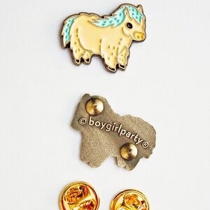 Op de afbeelding: Emaille pin met een cartoon gele pony met een blauwe en groene manen en staart. De pin heeft een gouden afwerking en is bevestigd aan een gouden metalen achterkant met een veiligheidsspeld. De achterkant is gestempeld met de tekst "&copy;boygirlparty&reg;".
