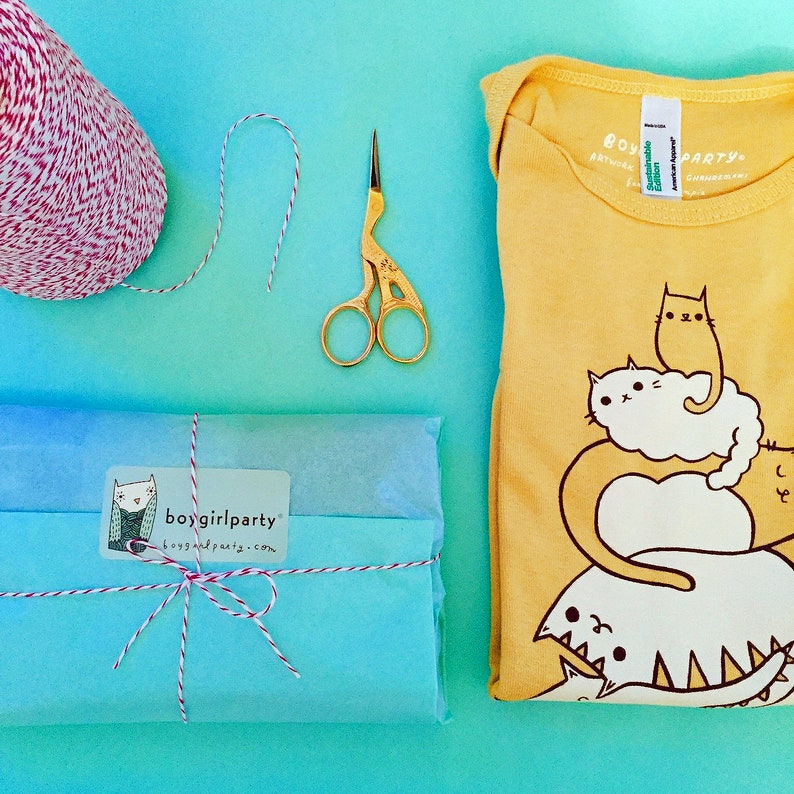 May include: A yellow onesie with a graphic of a stack of cats. The text "boygirlparty" is printed on a white sticker on a blue package wrapped with twine.
