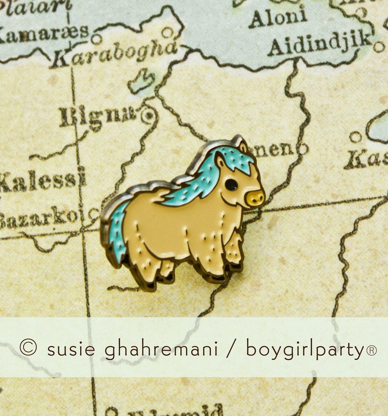 Op de afbeelding: Een kleine, lichtbruine emaille pin van een cartoon pony met een blauwe manen en staart. De pin is op een vintage kaart met de tekst "Karabogha" en "Aidindijk" zichtbaar.