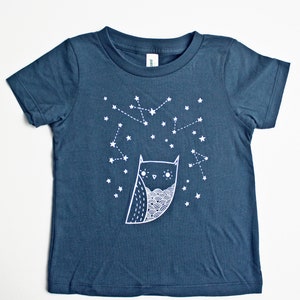 May include: A dark blue organic toddler tee with a white owl and constellation design. The text "organic toddler tee" is printed at the top of the image. The text "susie ghahremani / boygirlparty&reg;" is printed at the bottom of the image.