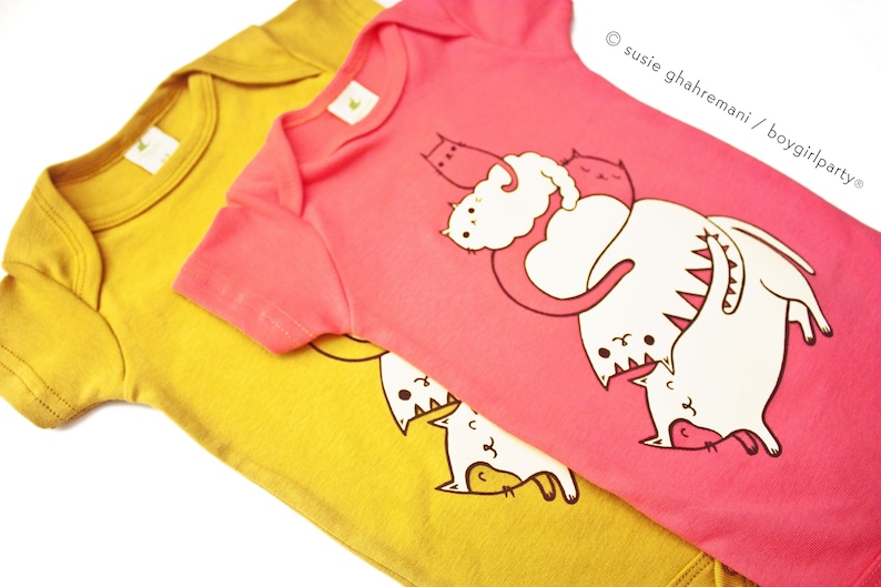May include: Two baby onesies, one yellow and one pink. The pink onesie has a graphic of cats playing. The yellow onesie has a graphic of cats playing.