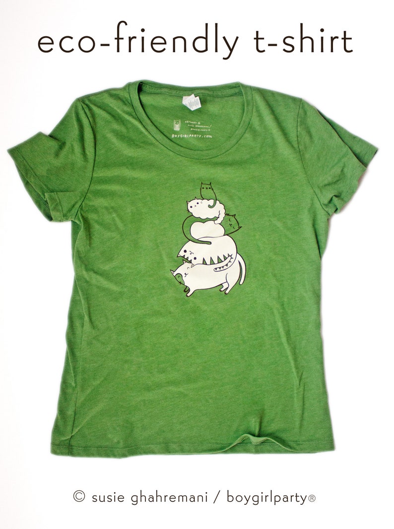 K&ouml;nnte beinhalten: Gr&uuml;nes, umweltfreundliches T-Shirt mit einem Aufdruck von f&uuml;nf &uuml;bereinander gestapelten wei&szlig;en Katzen mit gr&uuml;nen Akzenten. Der Text "susie ghahremani / boygirlparty&reg;" befindet sich am unteren Rand des Shirts.