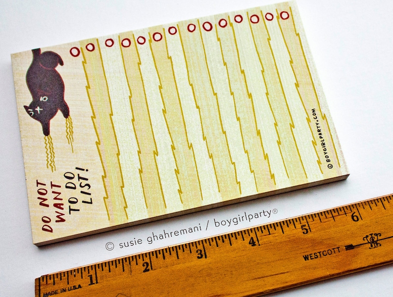 May include: A yellow notepad with a black cat illustration and the text "DO NOT WANT TO DO LIST!" printed on it. The notepad has a red border and a line of red circles at the top.