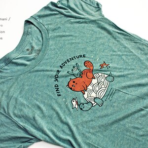 May include: Teal blue t-shirt with a graphic of a cat riding a turtle with the text "Find Your Adventure".
