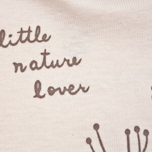 May include: White fabric with brown text that reads "little nature lover". The fabric has a subtle texture and is decorated with small brown floral designs.