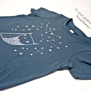May include: A dark blue t-shirt with a white owl and constellation design. The text "susie ghahremani / boygirlparty&reg;" is printed on the right side of the shirt.