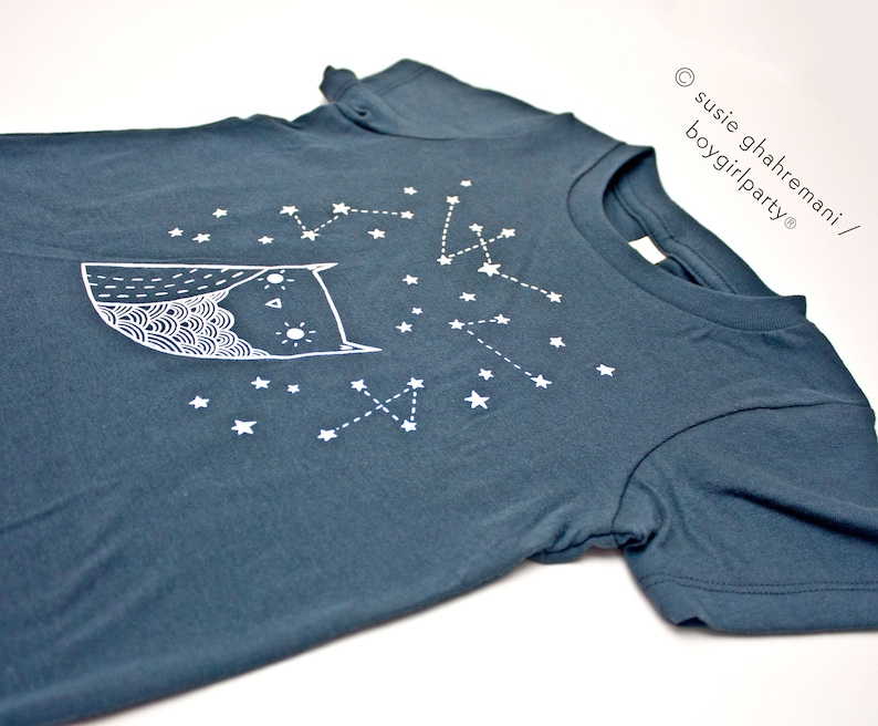 May include: A dark blue t-shirt with a white owl and constellation design. The text "susie ghahremani / boygirlparty&reg;" is printed on the right side of the shirt.