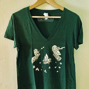 May include: A dark green v-neck t-shirt with a white graphic of three owls around a campfire. The text "boygirlparty.com" is printed on the shirt.