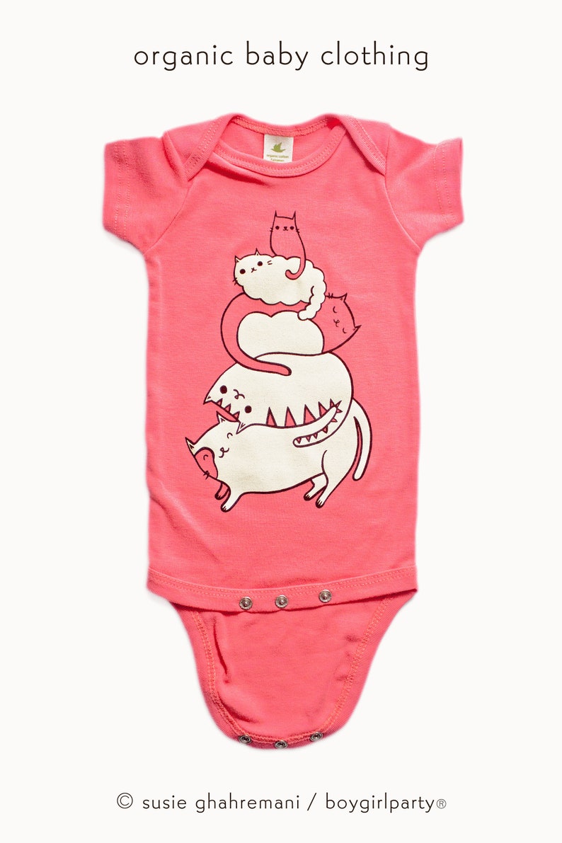 May include: Pink organic cotton baby onesie with a graphic of a stack of four cats. The cats are white with black outlines and are stacked on top of each other. The text "susie ghahremani / boygirlparty&reg;" is at the bottom of the onesie.
