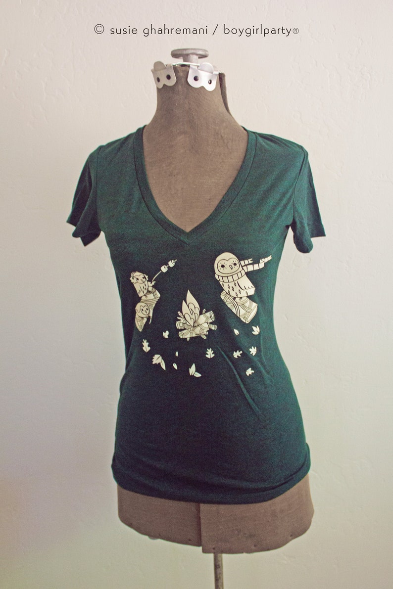 May include: A dark green t-shirt with a white graphic of owls around a campfire. The text "susie ghahremani / boygirlparty" is printed on the shirt.