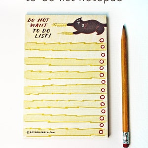 May include: A yellow notepad with a black cat illustration and the text "DO NOT WANT TO DO LIST!"  The notepad has a yellow lightning bolt pattern and red circles along the right edge.
