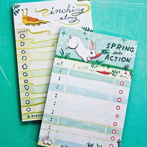 May include: Two green and blue notepad sets with illustrations. One notepad features a snail with the text "inching along" and the other notepad features a white rabbit with the text "Spring into Action".