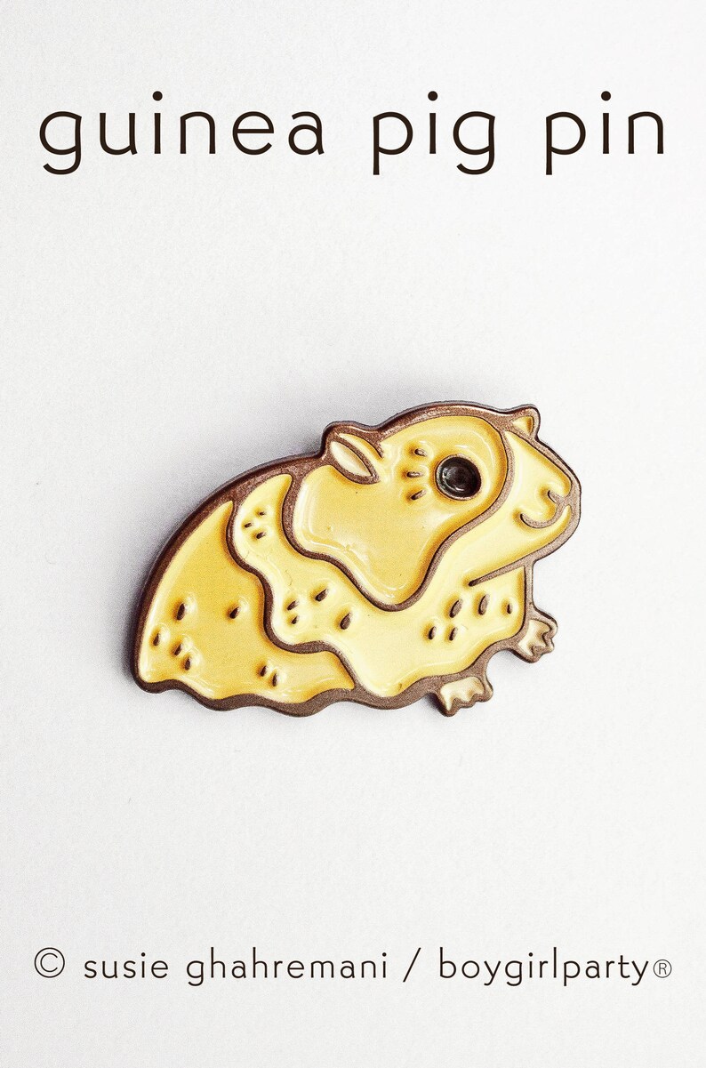 May include: A yellow enamel pin of a guinea pig. The pin has a brown outline and a black eye. The text "guinea pig pin" is above the pin.