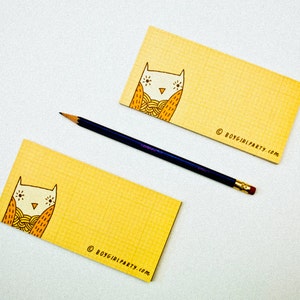 Op de afbeelding: Twee gele notitieblokken met een rasterpatroon en een illustratie van een uil met zijn ogen dicht. De uil draagt een gele en oranje sjaal. De tekst "&copy; boygirlparty.com" staat gedrukt op de onderkant van elk notitieblok.