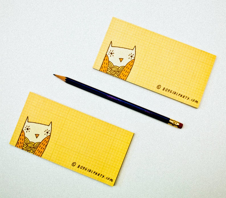 Op de afbeelding: Twee gele notitieblokken met een rasterpatroon en een illustratie van een uil met zijn ogen dicht. De uil draagt een gele en oranje sjaal. De tekst "&copy; boygirlparty.com" staat gedrukt op de onderkant van elk notitieblok.
