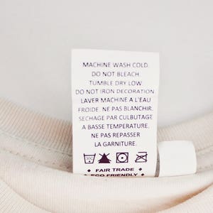 May include: White care label with instructions for machine washing, tumble drying, and ironing. The label also includes the text "Fair Trade" and "Eco Friendly".