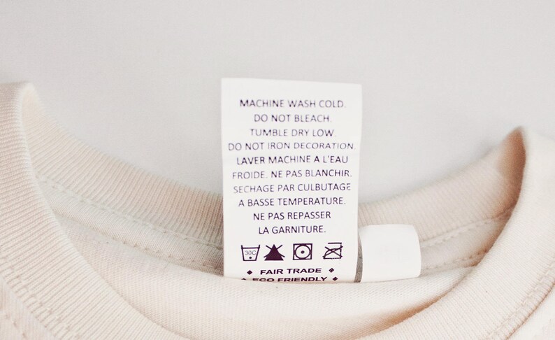 May include: White care label with instructions for machine washing, tumble drying, and ironing. The label also includes the text "Fair Trade" and "Eco Friendly".
