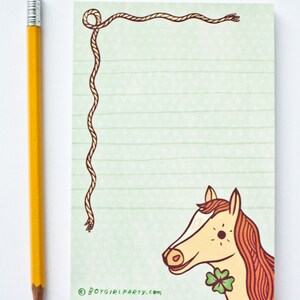 Op de afbeelding: Een groen en wit gestreept notitieboekje met een bruine touwrand en een cartoonpaard met een klavertje vier op zijn nek. Het notitieboekje heeft de tekst "&copy; BOYGIRLPARTY.com" onderaan.