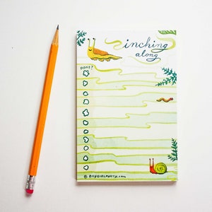 May include: A green and white to-do list notepad with a snail and slug illustration. The notepad has the text "inching along" and "DONE?" with a check box. The notepad is on a white background.