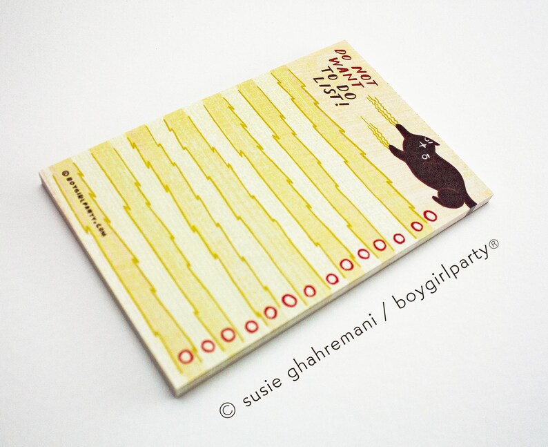 May include: A yellow and white notepad with a black cat illustration and the text "Do not want to do list". The notepad has red circles around the edges and the text "susie ghahremani / boygirlparty" at the bottom.