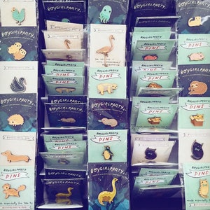 May include: A collection of colorful enamel pins featuring various animal and nature-themed designs. The pins are displayed on a white background with the text "BOYGIRLPARTY" and "PINS" on several of the cards.